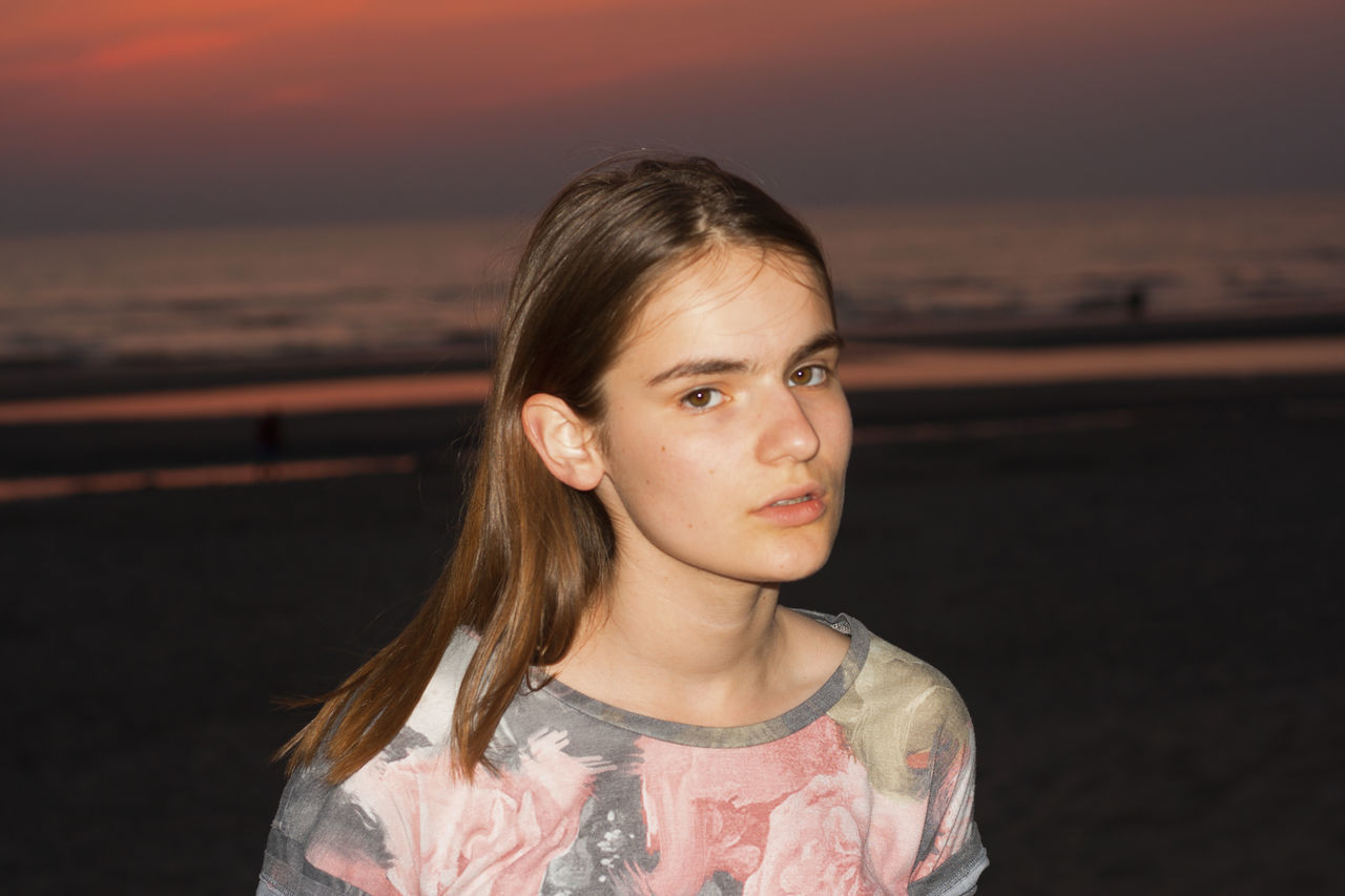 portrait, sky, looking at camera, headshot, front view, lifestyles, one person, sunset, leisure activity, real people, sea, water, childhood, women, casual clothing, females, hairstyle, contemplation