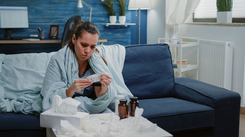 Sick woman holding medicine resting on sofa at home