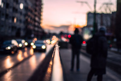 Defocused image of silhouette people on footpath by road in city