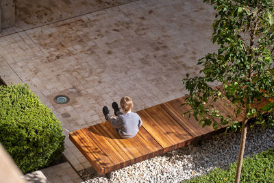 Overhead view of an outdoor setting with a boy sitting on a wooden bench. 