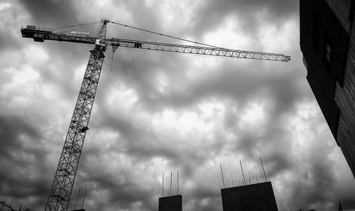 Low angle view of cranes at construction site against sky