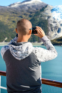 Man photographing with mobile phone by sea against mountain