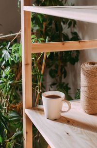 Close-up of coffee cup on shelf by plant