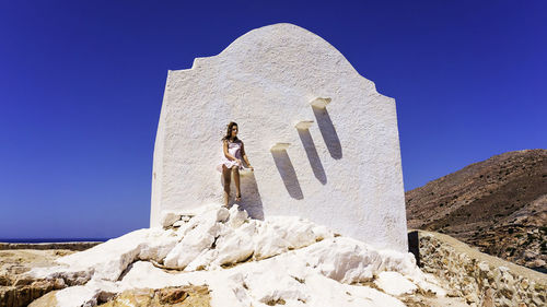 Teenage girl sitting on wall of white chapel during sunny day