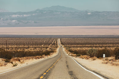 Country road along landscape and mountains against sky