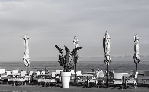 Chairs and tables on beach against sky