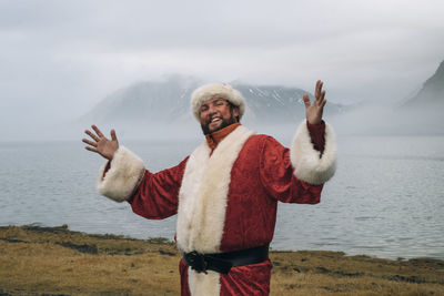 Man in santa costume standing against lagoon during winter