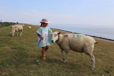 Full length of girl and sheep on field against sky