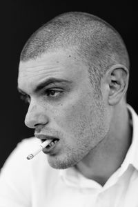 Close-up of young man smoking against black background