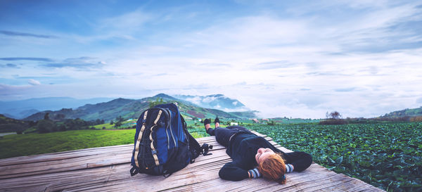 Rear view of man sitting on mountain against sky