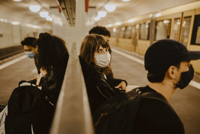 Young woman with friends sitting at subway station during pandemic
