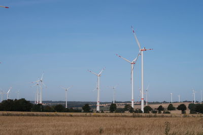 Windmills on field against clear blue sky