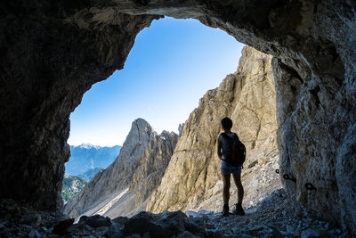 Rear view of woman with backpack standing in cave by mountains