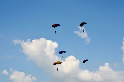 Low angle view of people paragliding against blue sky
