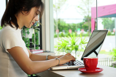 Young woman holding credit card while using laptop at home