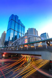 Light trails on modern buildings in city against blue sky