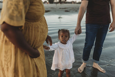 Toddler girl holding hands with parents in the water