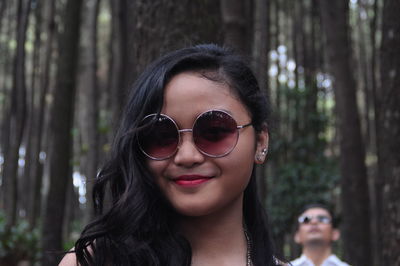 Portrait of smiling young woman wearing sunglasses at forest