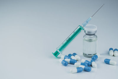 Close-up of pills and syringe against white background