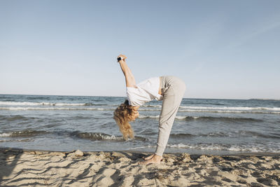 Woman with blond hair practicing stretching exercise on beach