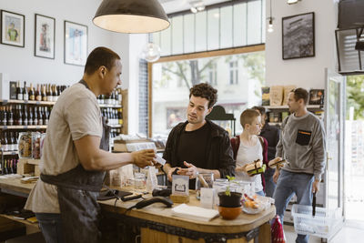 Side view of male owner explaining product to customer at checkout counter in store