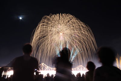 Rear view of people watching firework display at night