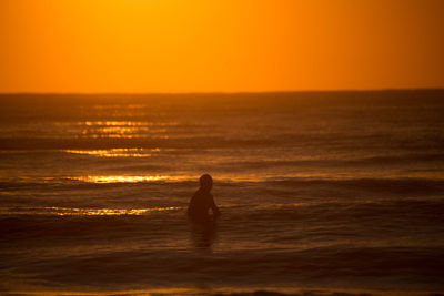 Silhouette surfer surfing in sea against sky during sunset