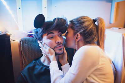 Young woman kissing a young man wearing mickey mouse ears