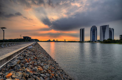 City by river against sky during sunset