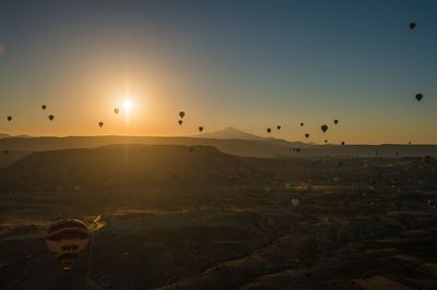 Hot air balloons flying over landscape against sky during sunset