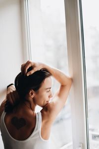 Young woman looking through window at home