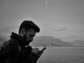 Side view of man using mobile phone by lake against sky