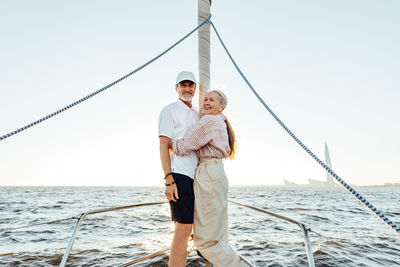 Smiling senior couple embracing in sailboat against sky