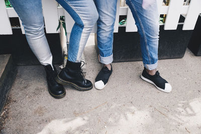 Low section of female friends wearing jeans while standing against fence