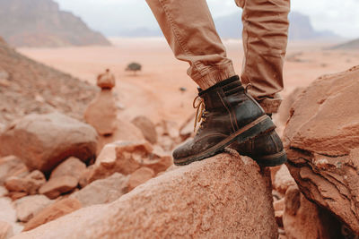 Legs of crop male tourist in hiking boots standing on rocks in wadi rum sandstone valley during holiday in jordan