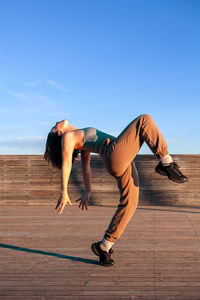 Full body of active female in sportswear bending back while warming up before training on stairs during outdoor workout in city