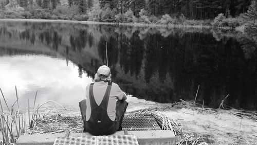 Rear view of man fishing while sitting at lakeshore