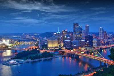 Illuminated city by river against sky at night