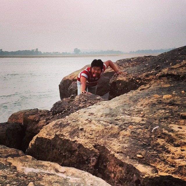 water, lifestyles, leisure activity, full length, sea, casual clothing, young adult, standing, clear sky, sitting, tranquility, rock - object, copy space, tranquil scene, person, scenics, rear view, nature