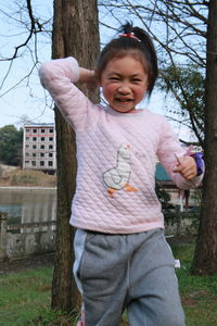 Portrait of happy girl standing on tree trunk