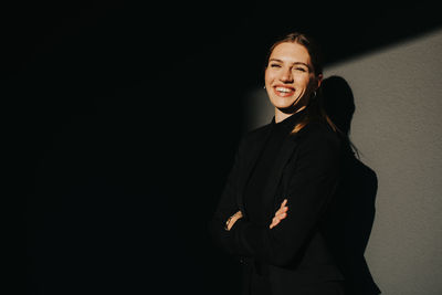 Portrait of smiling young woman standing against wall in darkroom