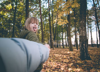 Cropped image of parent holding hands with daughter in forest during autumn