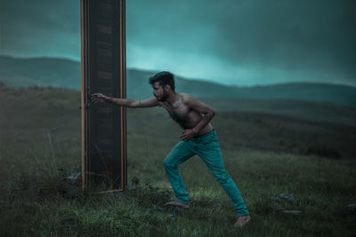 Full length of shirtless man standing on field against sky