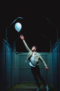 Young man hand reaching towards balloon at night