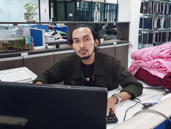 Portrait of young man using computer at table and looking at camera