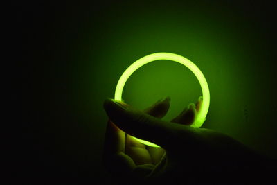 Close-up of woman holding glowing green bracelet in dark