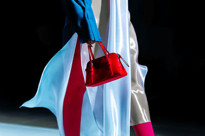 Fashionable details of a white silk dress and a red handbag in a woman's hand. elegant clothing 