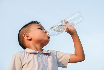 Low angle view of boy drinking water against sky