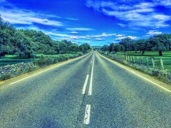 Empty road along trees and against sky