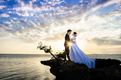 Couple kissing in sea against sky during sunset